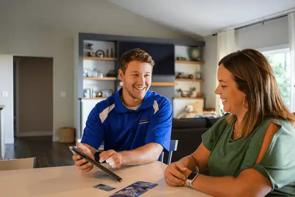 A man in a blue shirt shows a tablet to a woman in a green top at a table in a modern living room.